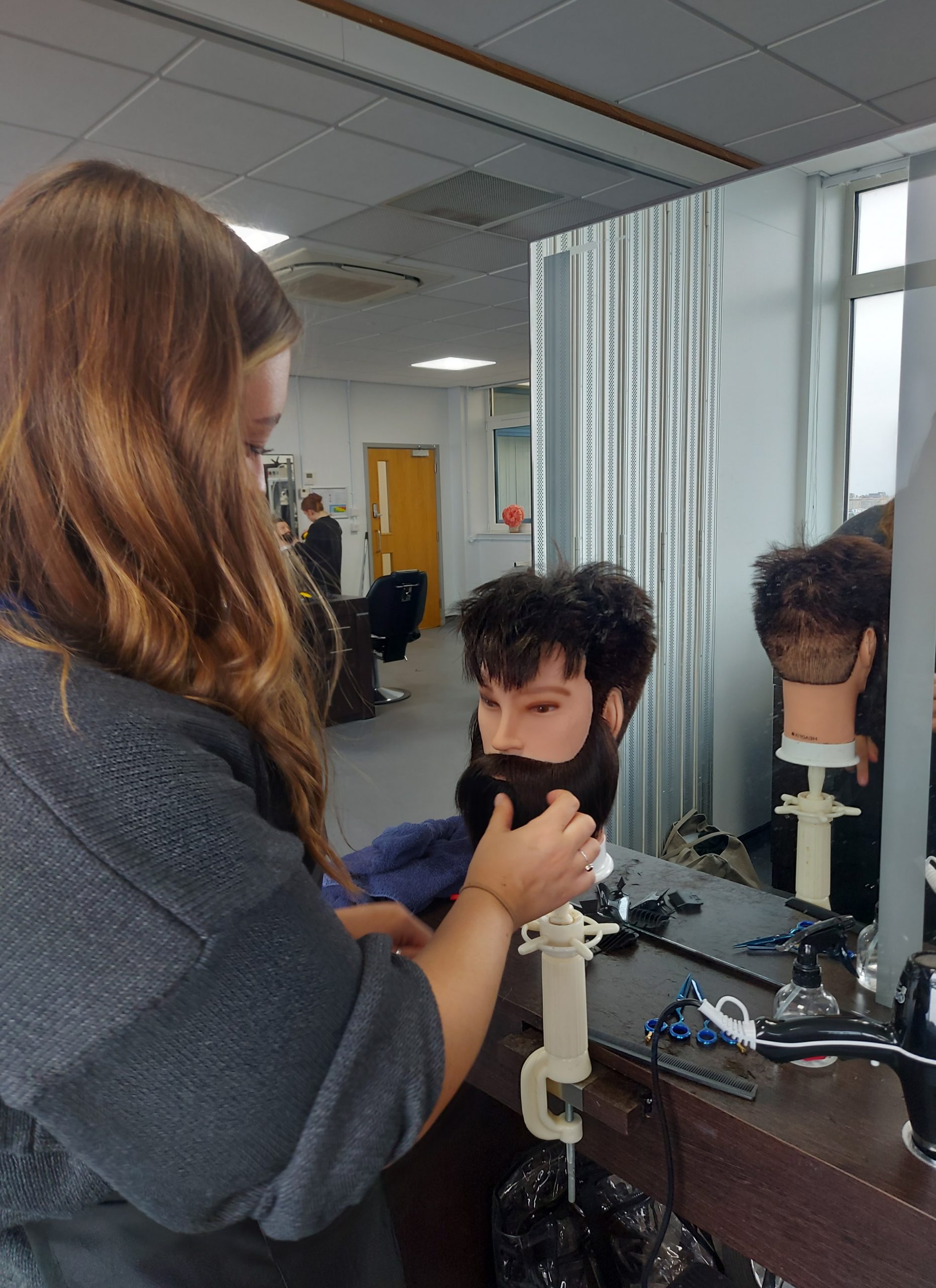 UCW student practicing barbering on a model head