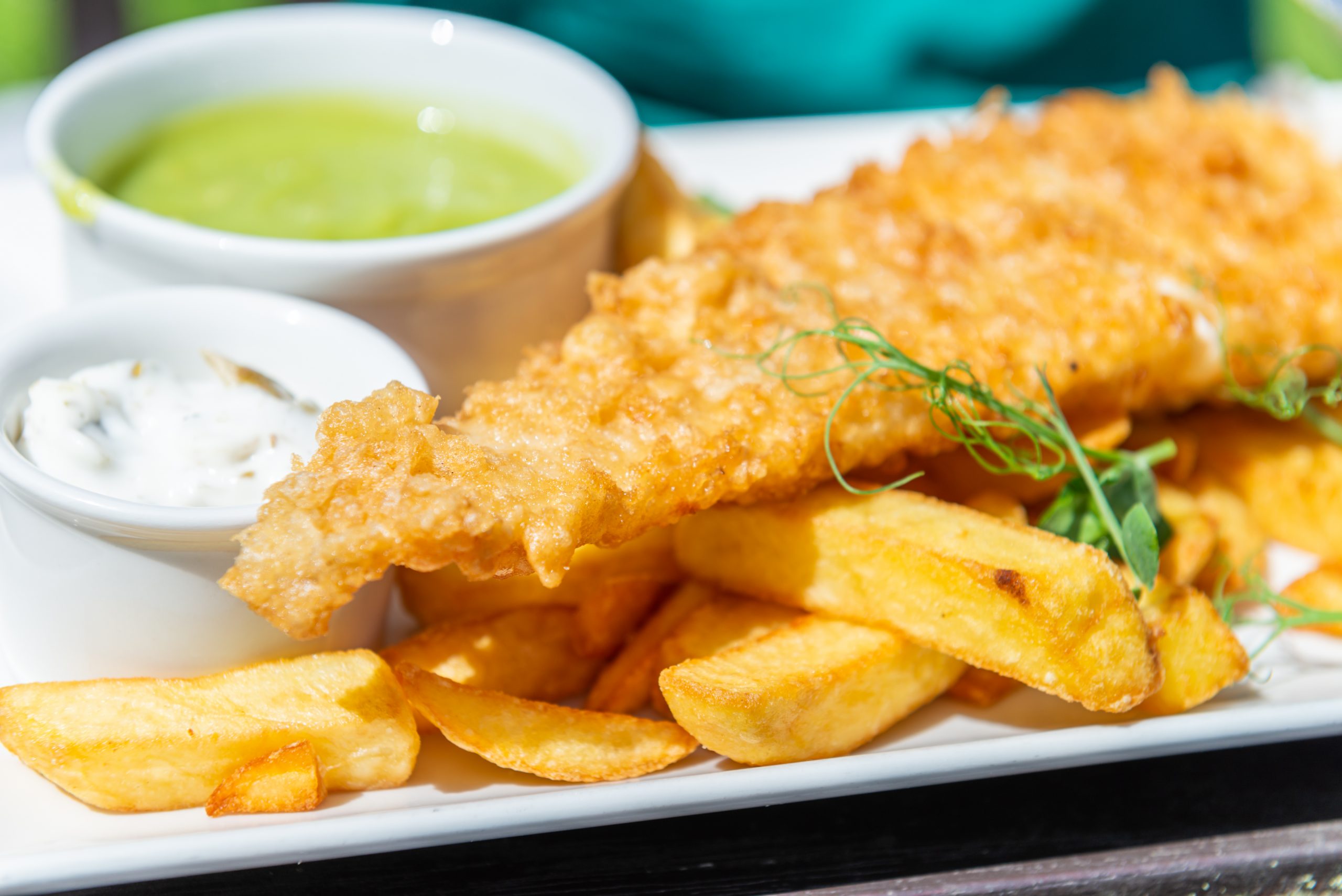 fish and chips on a plate with a pot of tartar sauce and mushy peas